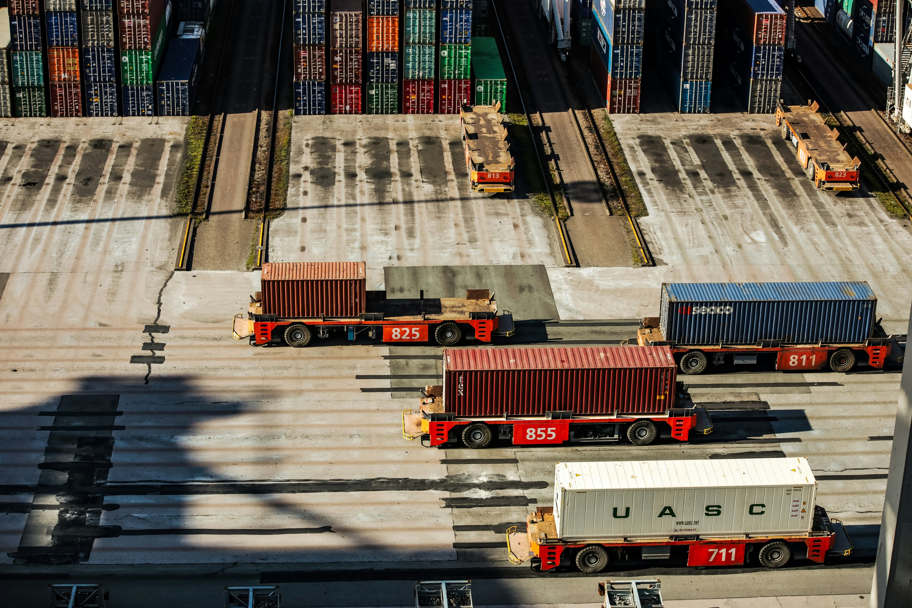 Aerial view of a busy container terminal with automated trucks transporting shipping containers between stacked cargo lanes.